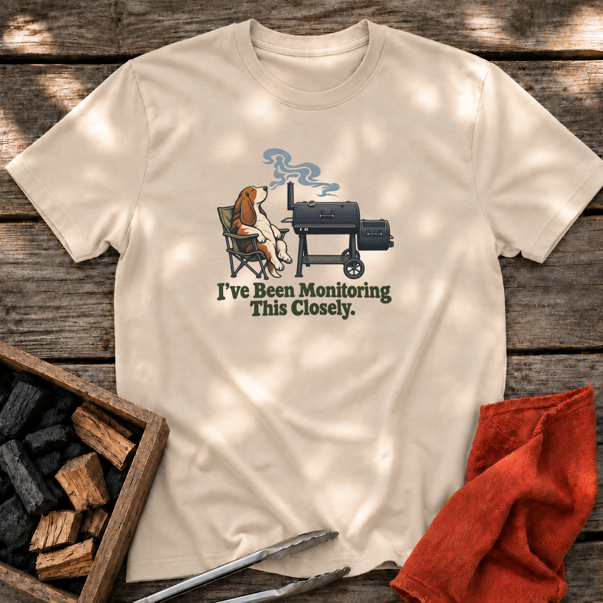 Sand T-shirt with the design “I've Been Monitoring This Closely.” printed on the front.