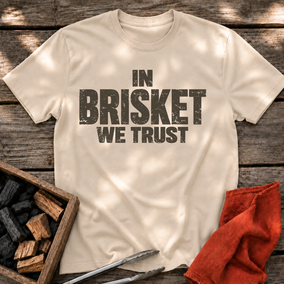 Sand T-shirt with the design “In Brisket We Trust.” printed on the front.
