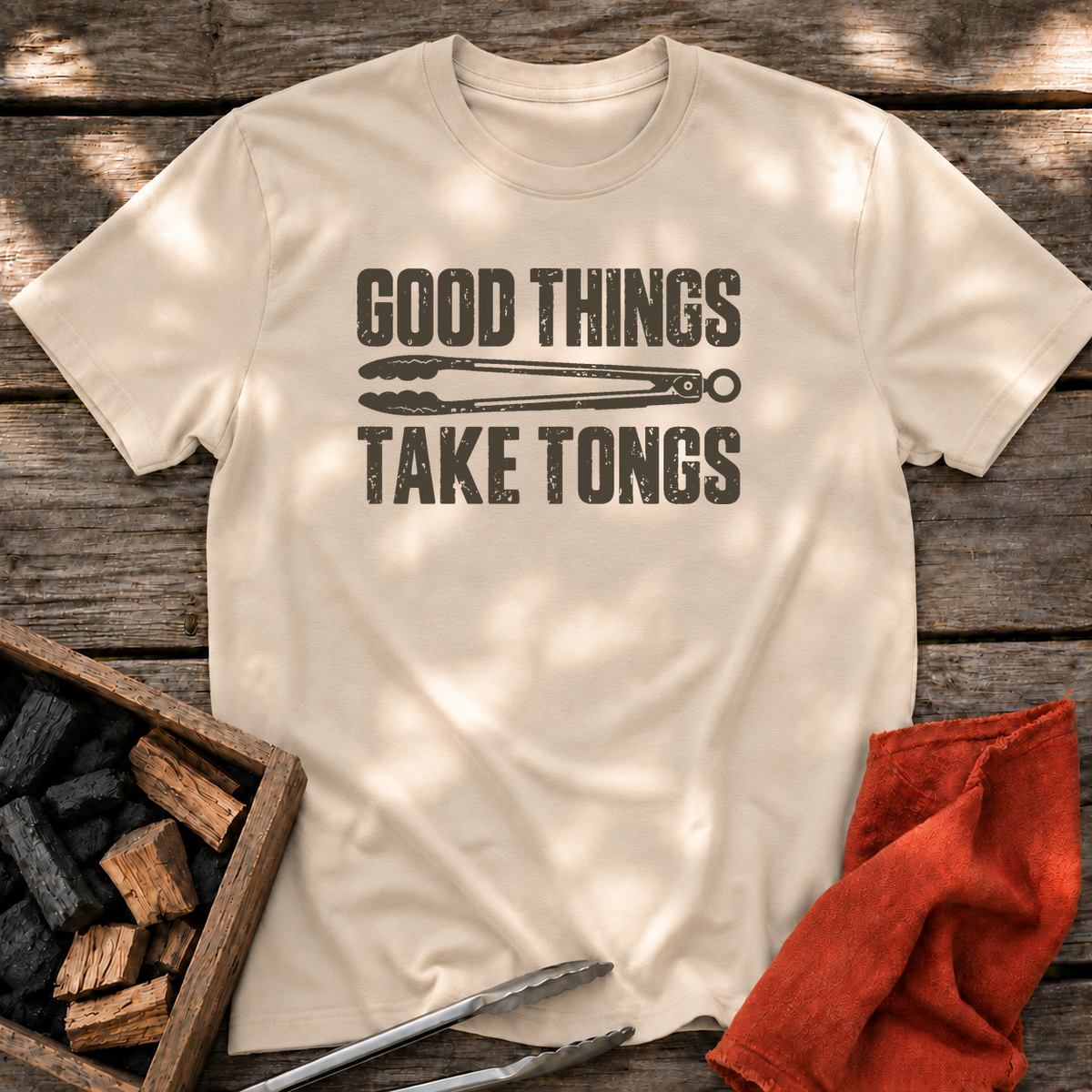 Sand T-shirt with the design “GOOD THINGS TAKE TONGS” printed on the front.