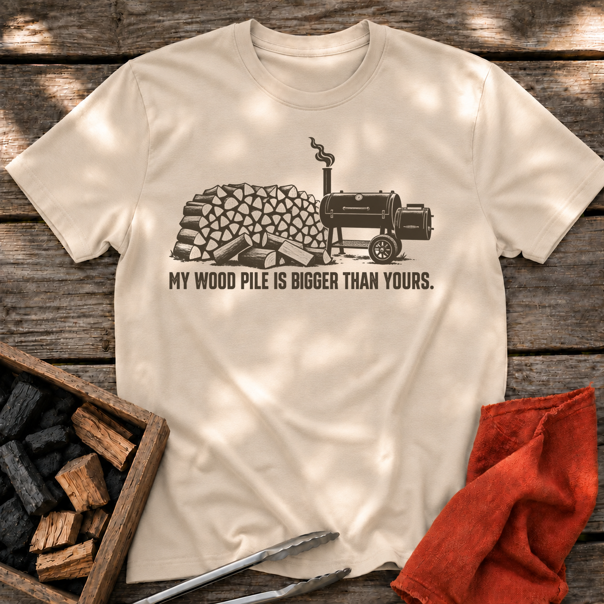 Sand T-shirt with the design “My Wood Pile is Bigger Than Yours” printed on the front.