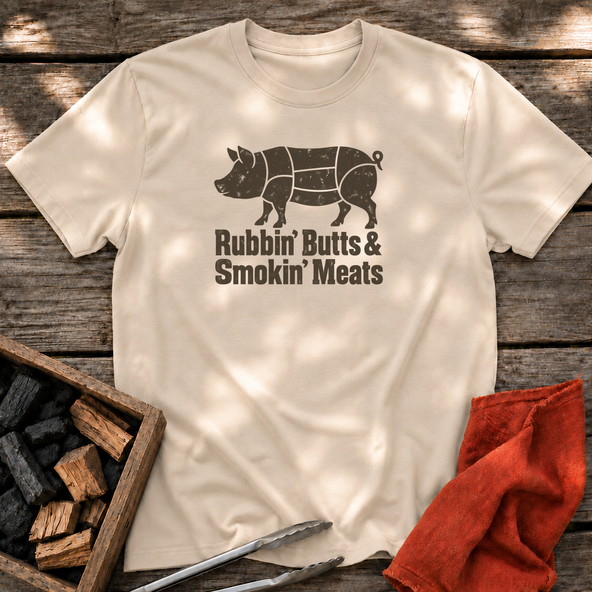 Sand T-shirt with the design “Rubbin' Butts & Smokin' Meats” printed on the front.