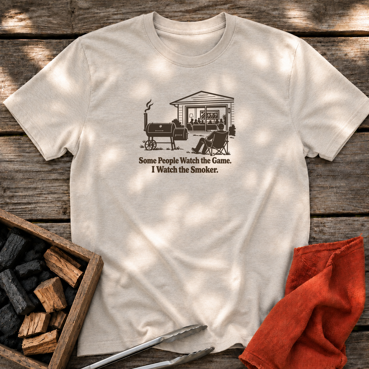Natural T-shirt with the design “Some People Watch the Game. I Watch the Smoker.” printed on the front.