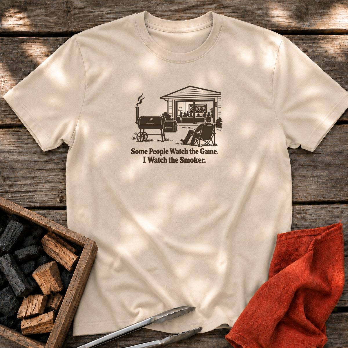 Sand T-shirt with the design “Some People Watch the Game. I Watch the Smoker.” printed on the front.