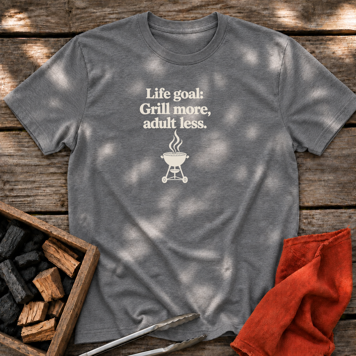 Graphite Heather T-shirt with the design “Life goal: Grill more, adult less.” printed on the front.