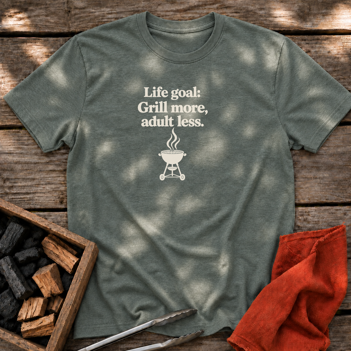 Heather Military Green T-shirt with the design “Life goal: Grill more, adult less.” printed on the front.