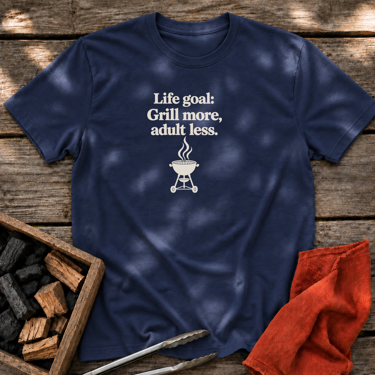 Navy T-shirt with the design “Life goal: Grill more, adult less.” printed on the front.
