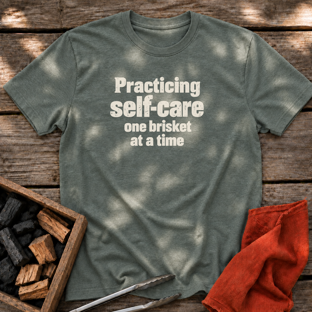 Heather Military Green T-shirt with the design “Practicing self-care one brisket at a time.” printed on the front.